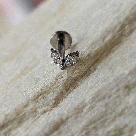 minimalistyczny labret z tytanu, ozdobiony dwiema cyrkoniami w szlifie markiza, osadzonymi pod kątem, co tworzy efekt subtelnego listka lub skrzydełek.