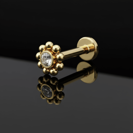 Labret zdobi biała cyrkonia w klasycznym, okrągłym szlifie – osadzona tak, aby pięknie odbijała światło i mieniła się niczym maleńki diament. Kamień otacza misterna ramka z drobnych, złotych kuleczek, które dodają całości lekkości i wyjątkowego uroku.