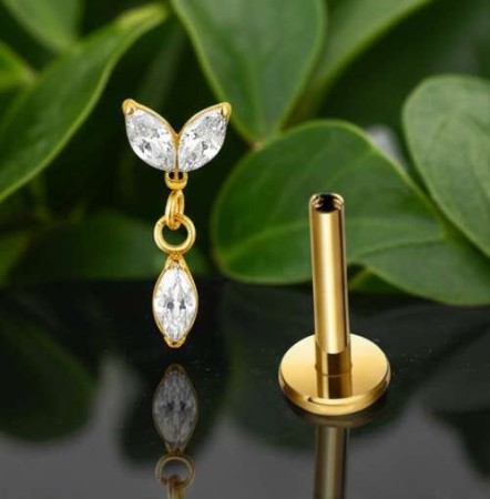 Elegancki labret z ruchomą zawieszką w luksusowym złotym wykończeniu PVD. Centralnym elementem jest podwójny kryształowy listek wykonany z dwóch białych cyrkonii, od którego odchodzi łańcuszek z dwoma ogniwami, zakończony cyrkoniową łezką