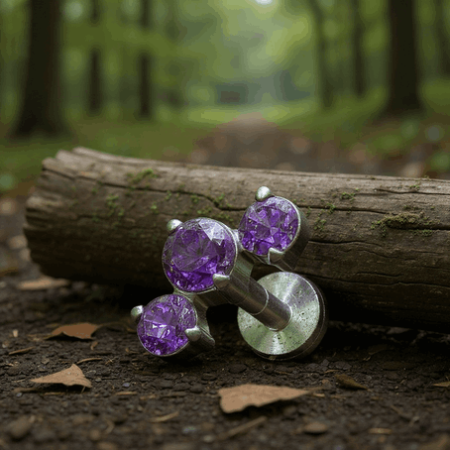 Subtelny i stylowy labret o delikatnie łukowatej formie, ozdobiony trzema fioletowymi cyrkoniami kubicznymi osadzonymi w eleganckiej oprawie łapowej (krapowej).