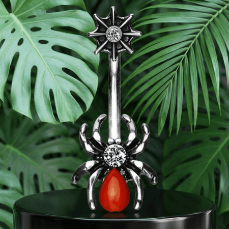 Kolczyk do pępka z oryginalnym motywem pająka – korpus ozdobiony białą cyrkonią, pomarańczowo-czerwony brzuch i efektowna pajęczyna. Pręt ze stali chirurgicznej, ozdobna część z mosiądzu pokryta rodem. Zewnętrzny gwint.