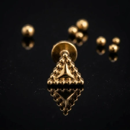 Elegancki złoty labret w kształcie trójkąta z wytłoczonymi koralikami na obwodzie to minimalistyczna biżuteria z dekoracyjnym akcentem.