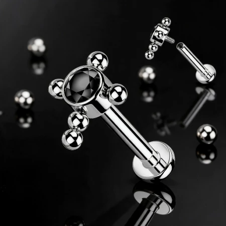 Wyrazisty labret tytanowy z ozdobną nakrętką w kształcie krzyżyka to propozycja dla osób, które cenią oryginalną biżuterię z charakterem. Krzyżyk złożony z drobnych kuleczek został ozdobiony czarną cyrkonią, która nadaje  nieco mrocznego wyglądu.
