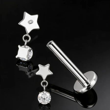 Star Crystal Dangle łączy niewielką gwiazdkę z geometrycznym szlifem i subtelnie zwisającą białą cyrkonię, tworząc lekką, biżuteryjną kompozycję.