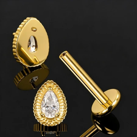 Tytanowy labret Hindu Drop Crystal w złotym wykończeniu PVD zachwyca ozdobą w kształcie gruszki, w której centralne miejsce zajmuje błyszcząca, biała cyrkonia.